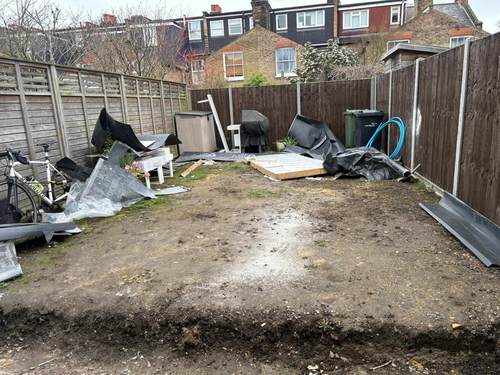 Cleared rear garden before work, bare earth with debris against old fencing
